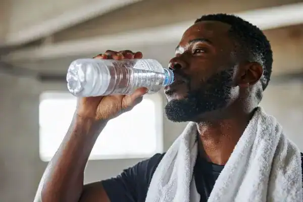 Image of man drinking water to improve hydration Hove after work out.